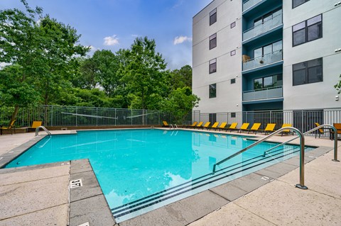 A swimming pool surrounded by a metal fence and yellow chairs.