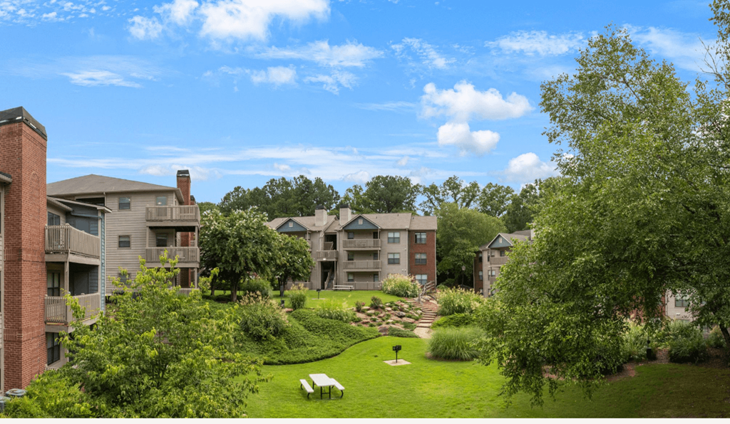 A grassy area with benches and trees in front of apartment buildings.