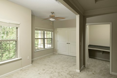 A room with a ceiling fan and a window with a view of trees.