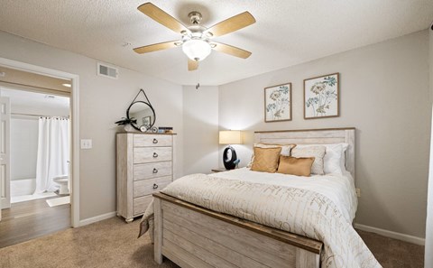 A bedroom with a bed, dresser, and a ceiling fan.