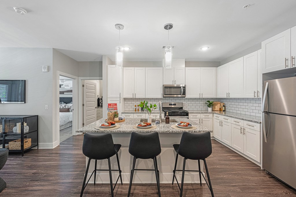 a kitchen with white cabinets and a granite island with four chairs