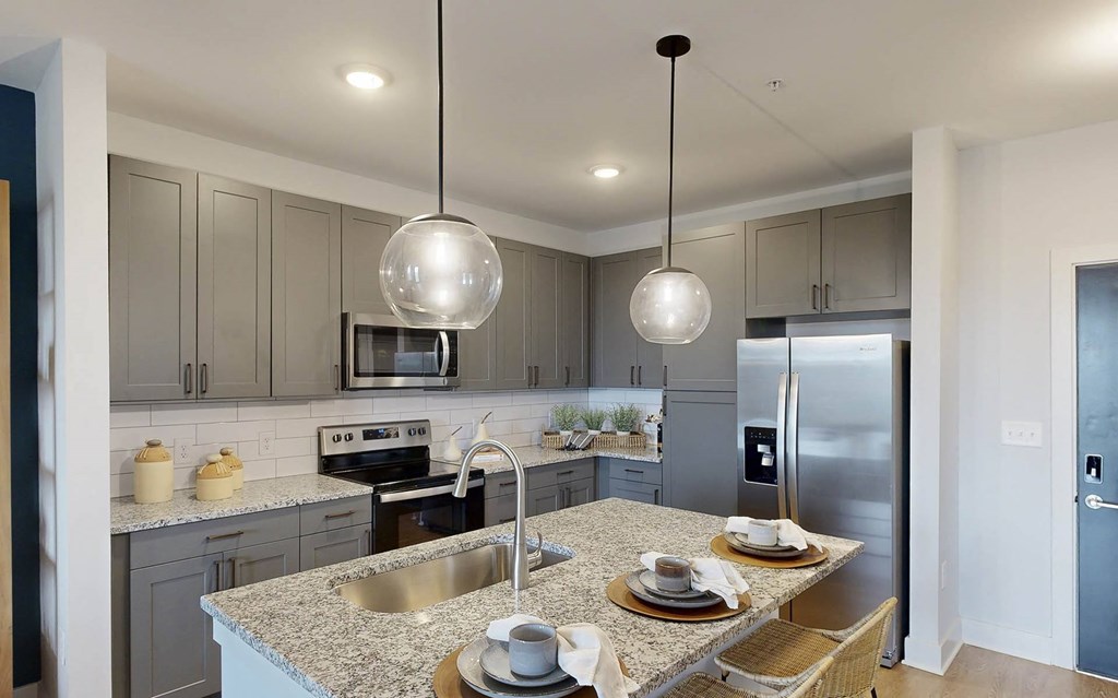 Pet-Friendly Apartments in Madison, Alabama - The Dempsey - Kitchen with Gray Cabinetry, Stainless Steel Appliances, Granite Countertops, and Island with Pendant Lighting.