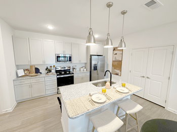 A kitchen with a table set for two with plates and glasses of orange juice.