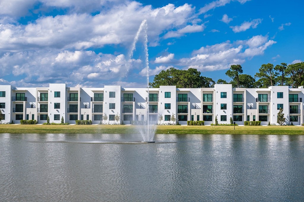 a fountain in the middle of a lake with an apartment building in the background at Altis Blue Lake, Lake Worth, Florida