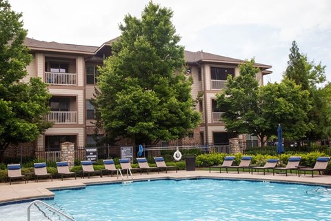 Dog-Friendly Apartments in Atlanta, GA - Gardens at Park Ridge Luxury Homes - Outdoor Pool With Lounge Chairs, Landscaped Trees, And Surrounding Apartment Buildings.
