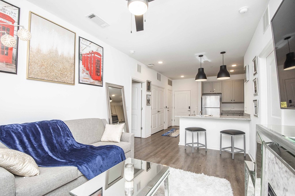 A modern living room with a grey couch and a kitchen in the background.