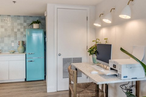a kitchen with a desk with a computer and a refrigerator