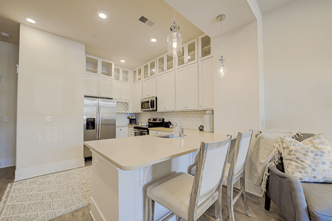 A kitchen with white cabinets and a large island with chairs around it.