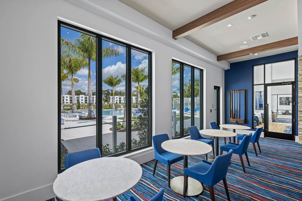 a lounge area with tables and chairs and large windows at Altis Blue Lake, Lake Worth, FL, 33467