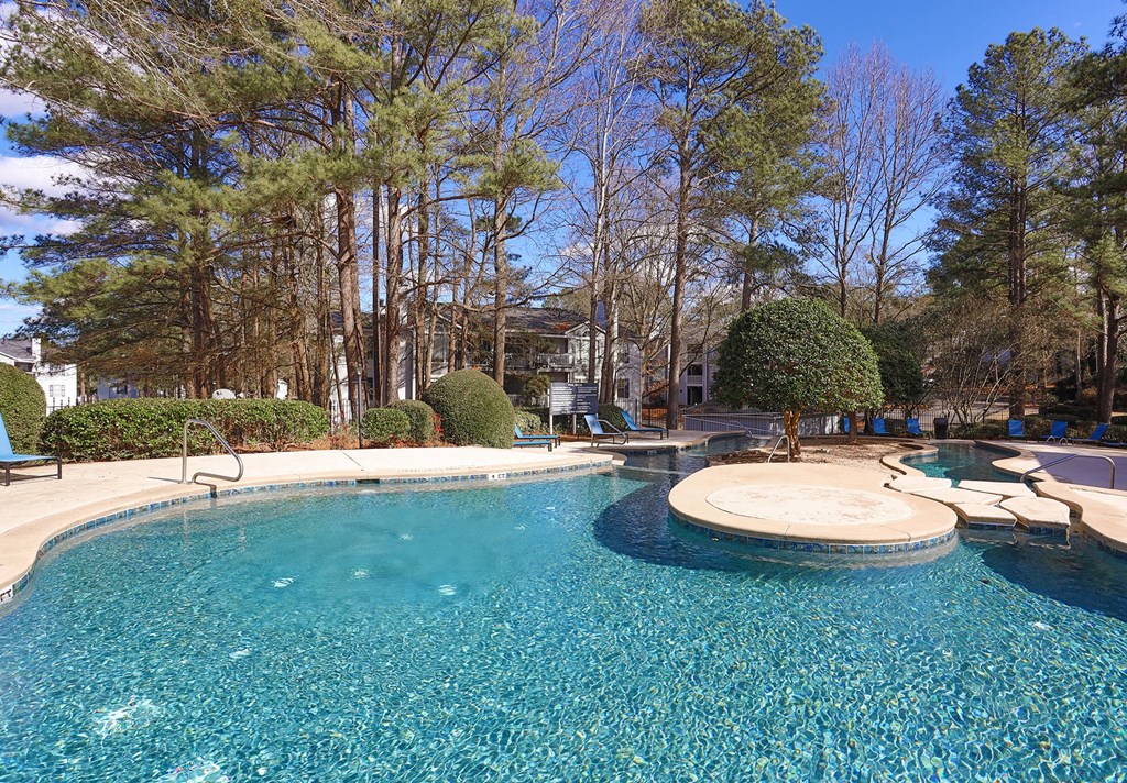a swimming pool with a patio and trees in the background