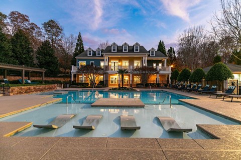 Newnan, GA, Apartments with In-Unit Washer and Dryer - The Jackson - Swimming Pool With In-Water Lounge Chairs, Spacious Sundeck, Clubhouse Building, And Evening Sky.