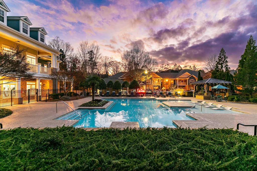 A large outdoor swimming pool surrounded by a grassy area and residential houses.