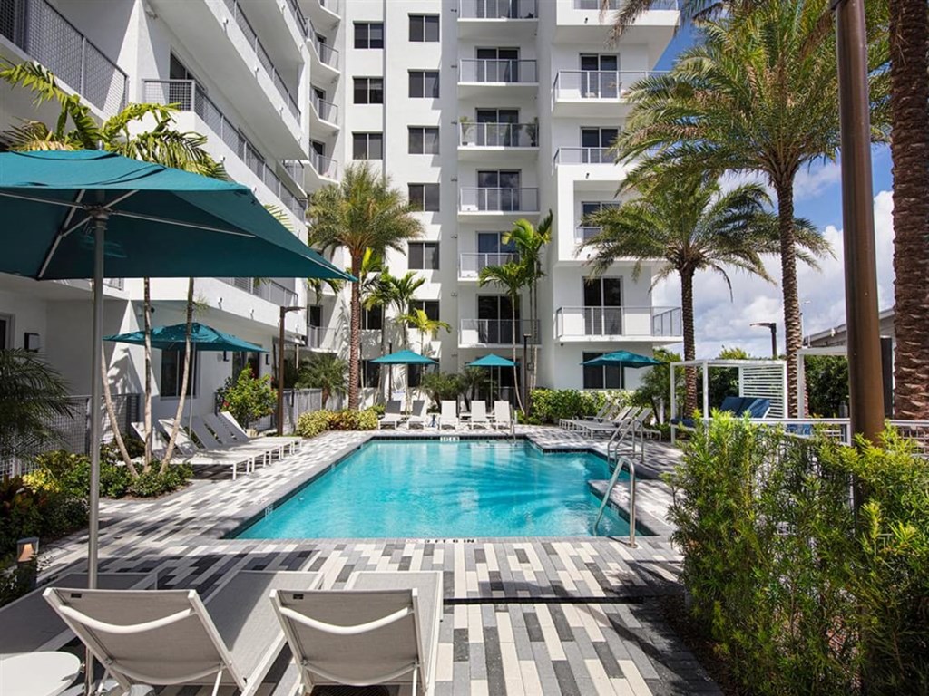 a large swimming pool with chaise lounge chairs and umbrellas in front of a white at Saba Pompano Beach, Pompano Beach, 33062