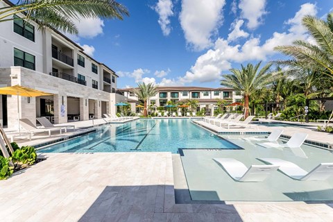 A large swimming pool with sun loungers in front of apartment buildings.
