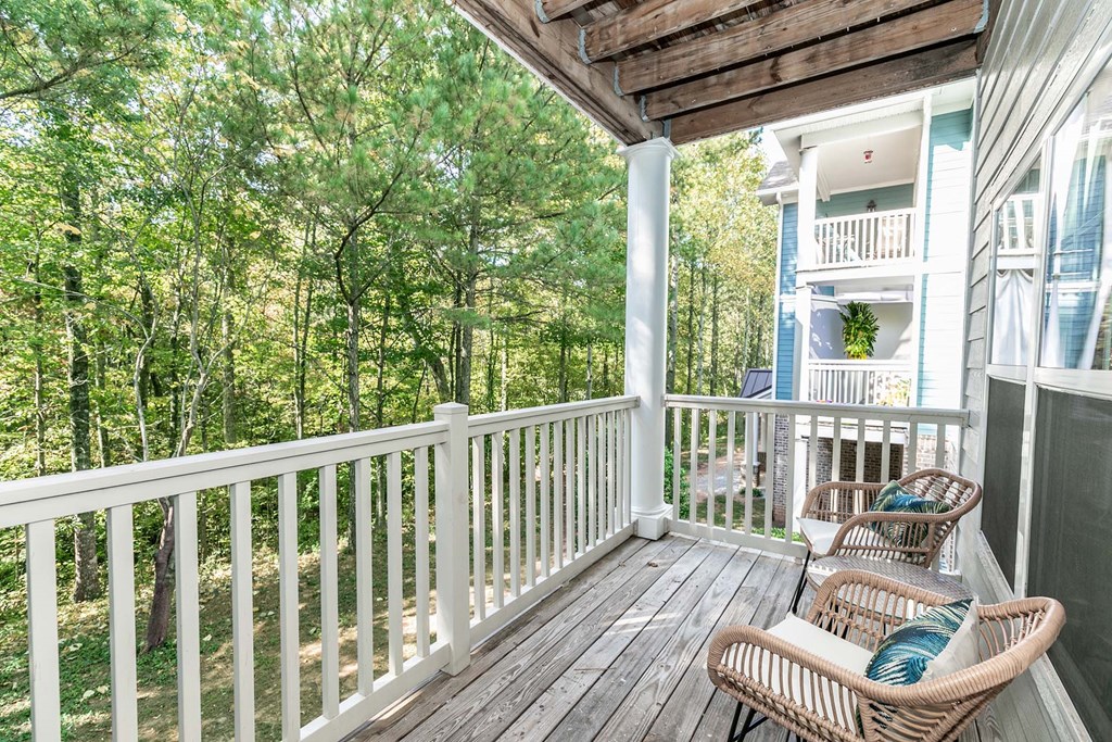 a porch with two wicker chairs and a view of trees