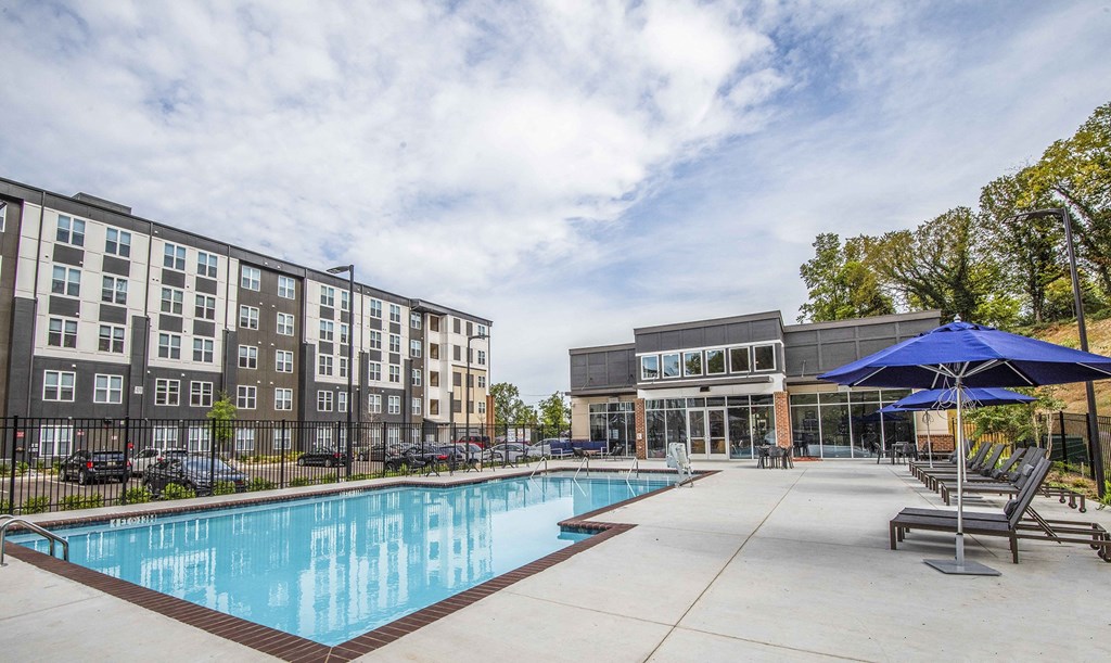 A swimming pool in front of a building with a blue umbrella.