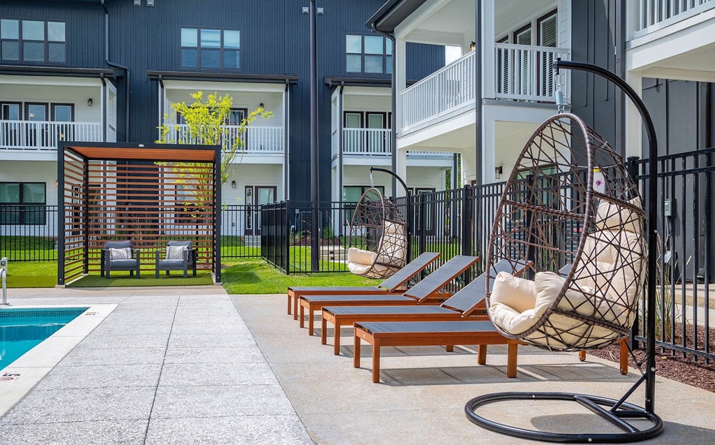 a patio with lounge chairs and a swing in front of an apartment building