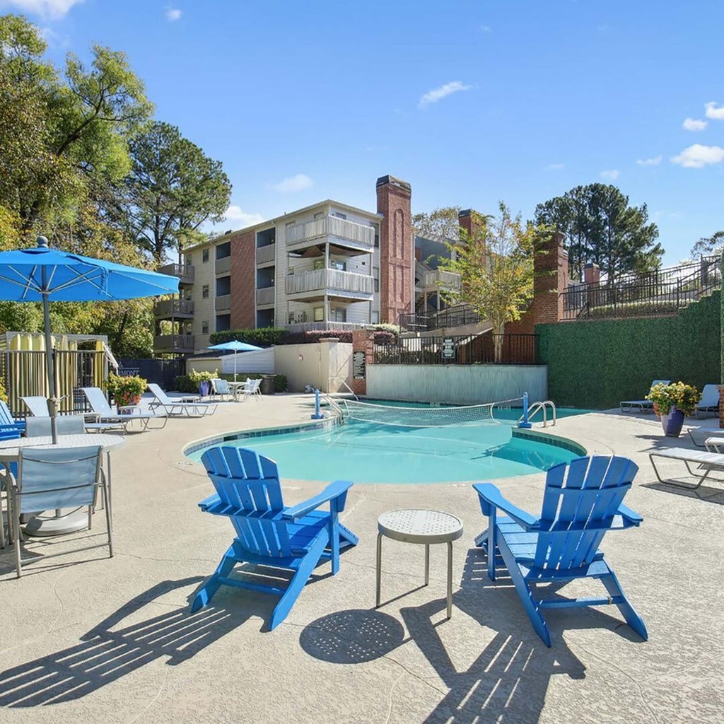 a pool with blue chairs and umbrellas next to a resort style swimming pool
