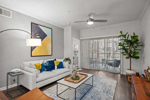 A living room with a white couch and a yellow and blue abstract painting on the wall.