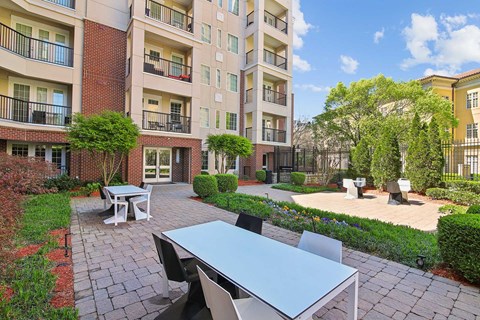 A patio with a table and chairs is surrounded by a brick building and greenery.