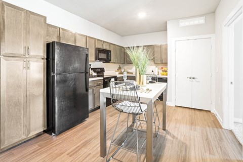 Fort Worth, TX, Senior Apartments Near Capp Smith Park - Regatta 55 - Kitchen With Designer Cabinetry, Black Appliances, Island Seating, and Hardwood-Style Flooring.