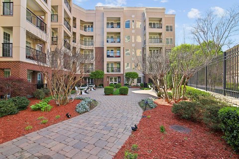 A brick walkway leads to a courtyard with a fence and trees.