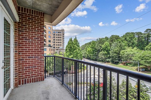 A balcony with a black railing overlooks a street with cars and trees.