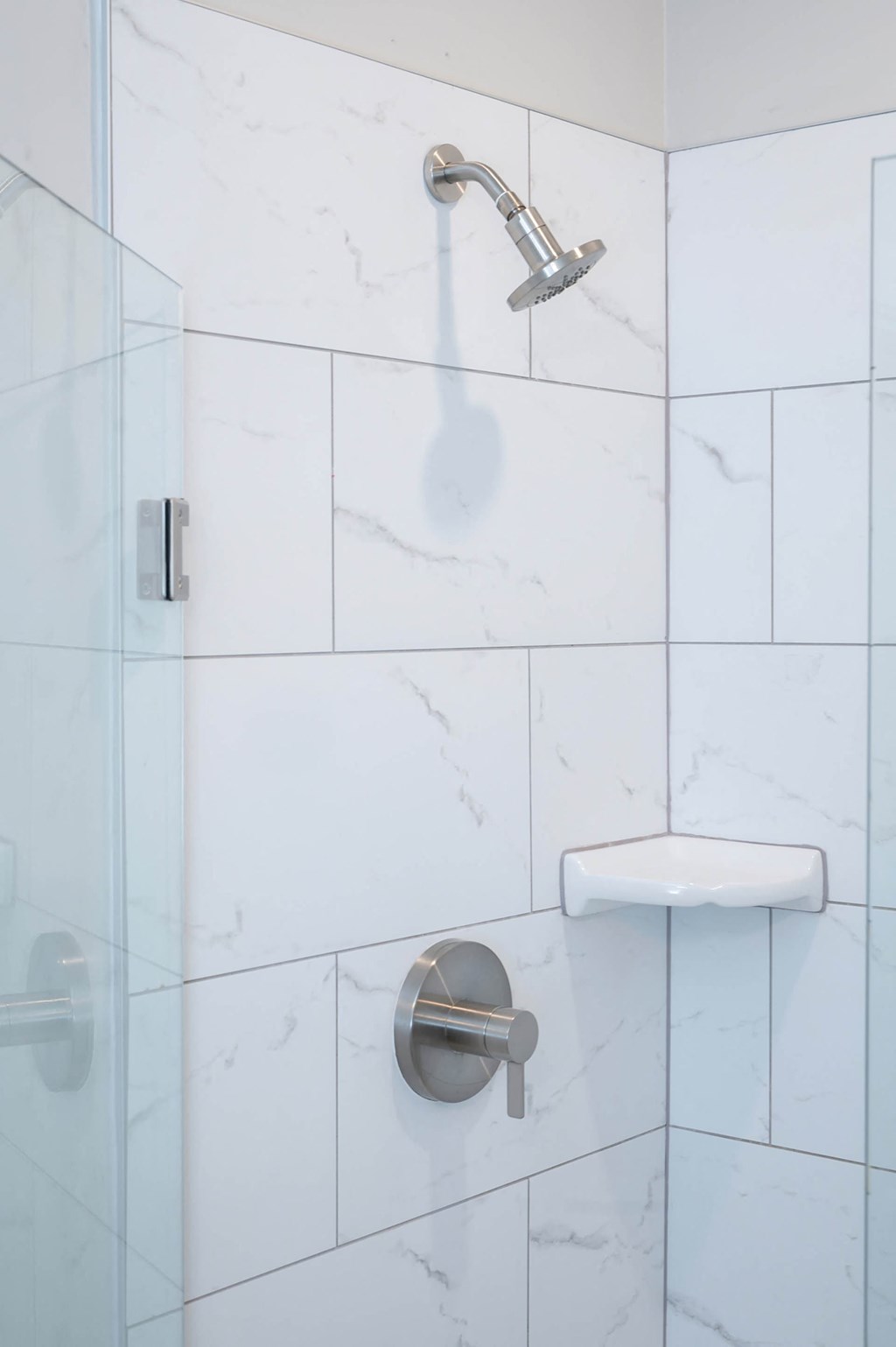a white tiled bathroom with a shower and a soap dispenser