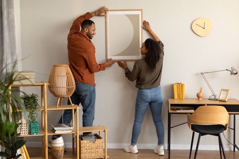 a man and a woman are hanging a mirror on a wall