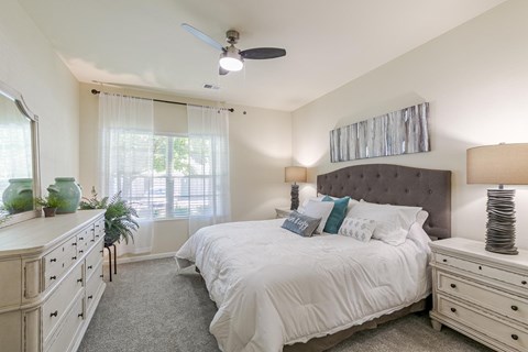 A bedroom with a large bed, a dresser, and a ceiling fan.