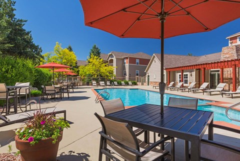 A poolside table with chairs and an umbrella overlooking a pool.