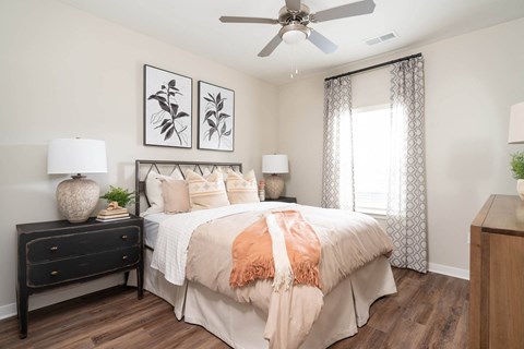 Dog-Friendly Luxury Apartments in Alcoa, TN - Vintage Hunters Crossing - Bedroom with a Bed, Hardwood-Inspired Flooring, Nightstands, Lamps, Wall Arts, Dresser, and Ceiling Fan with Lighting.
