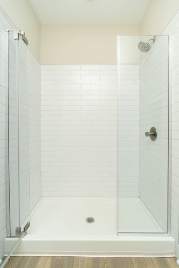 A white tiled shower with a glass door and a drain.