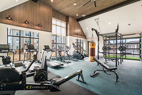 Johnson City, TN, Apartments with Fitness Center - Vintage Johnson City - Fitness Center With Cardio Machines, Rowing Equipment, Weight Rack, Bench, Punching Bag, Wood Ceiling, And Large Windows.