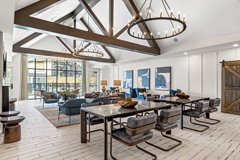Pet-Friendly Luxury Apartments in Johnson City, TN - Vintage Johnson City - Resident Lounge With Vaulted Ceilings, Exposed Beams, Modern Chandeliers, Dining Tables, And Comfortable Seating.