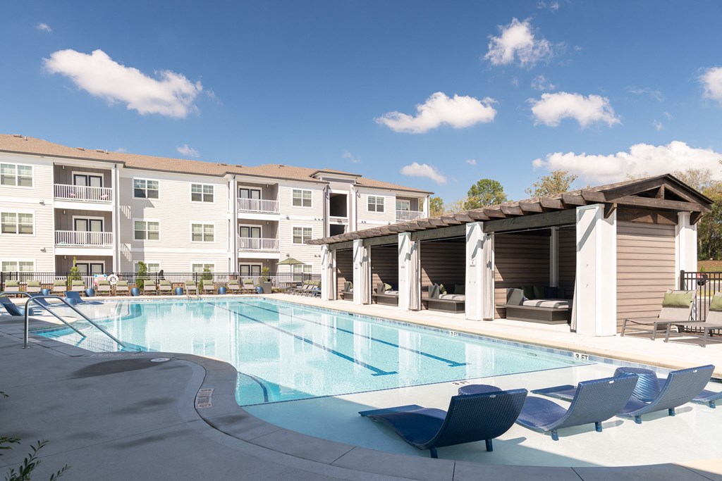a swimming pool with blue chairs and an apartment building in the background