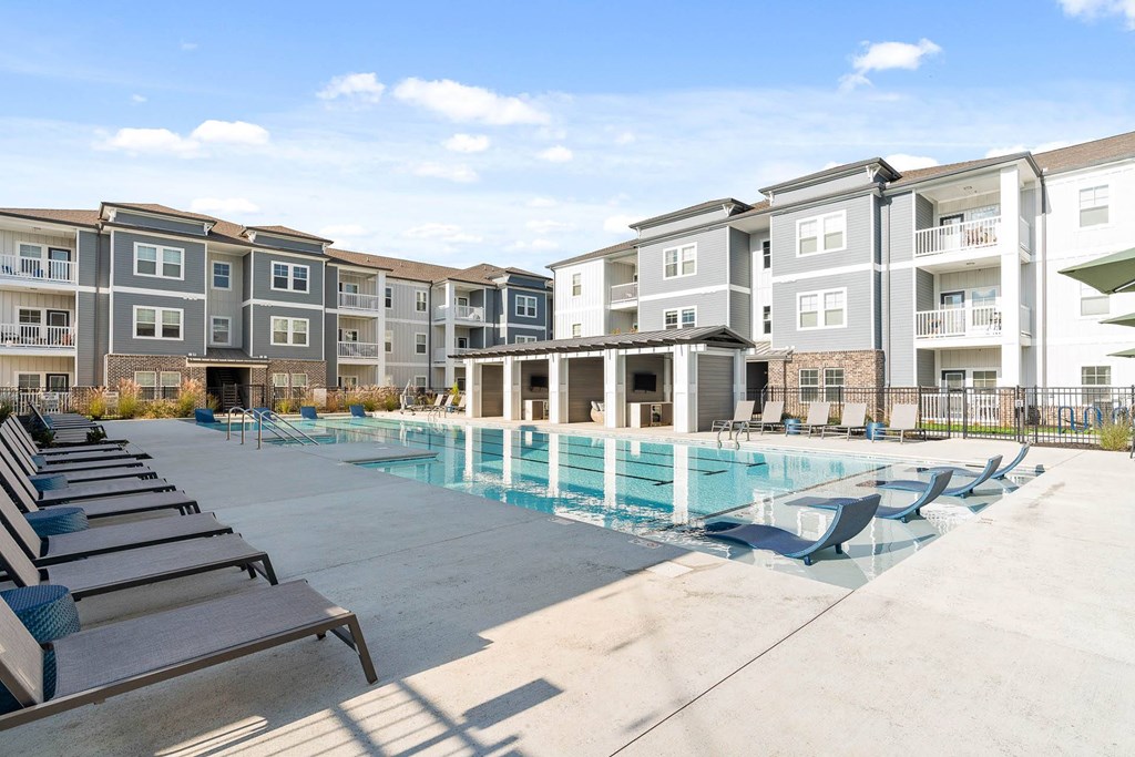 a swimming pool with chaise lounge chairs in front of an apartment building