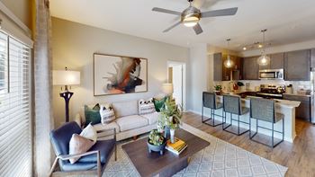 a living room with a ceiling fan and a kitchen in the background