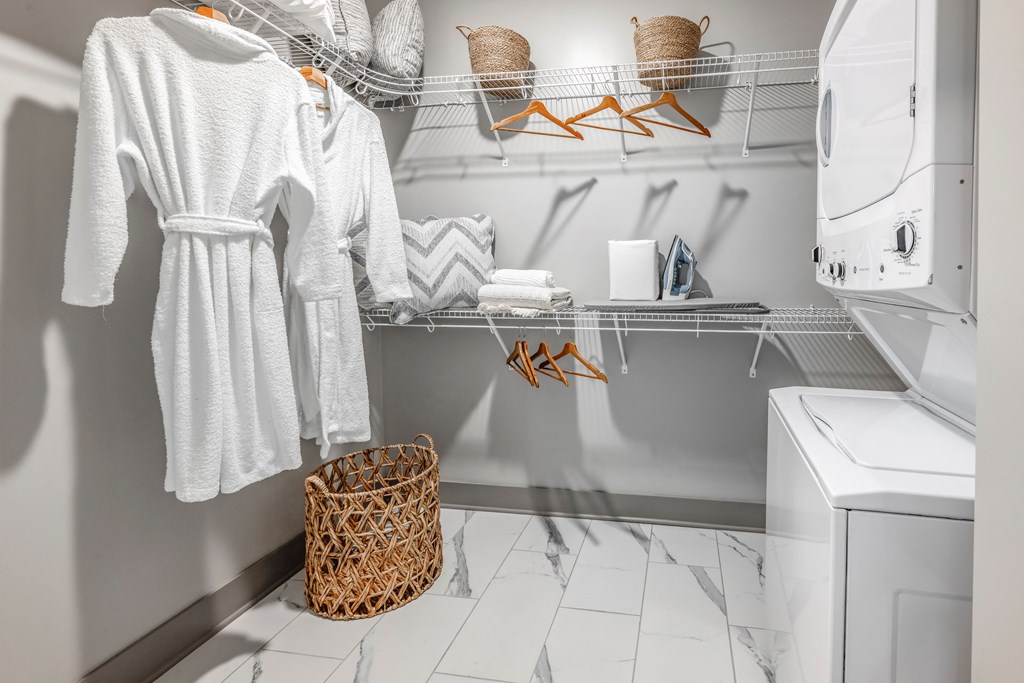 a small laundry room with white robes and a washing machine and a basket