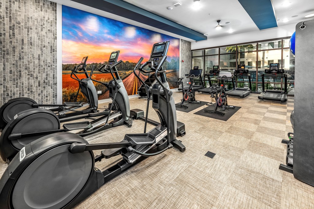 a gym with cardio equipment and a wall mural of a sunrise