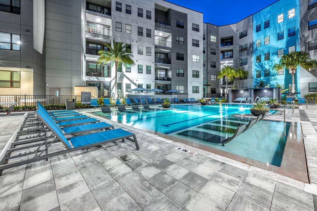 an apartment pool with blue lounge chairs in front of an apartment building