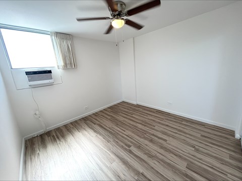 A room with a ceiling fan and a window with an air conditioner unit.