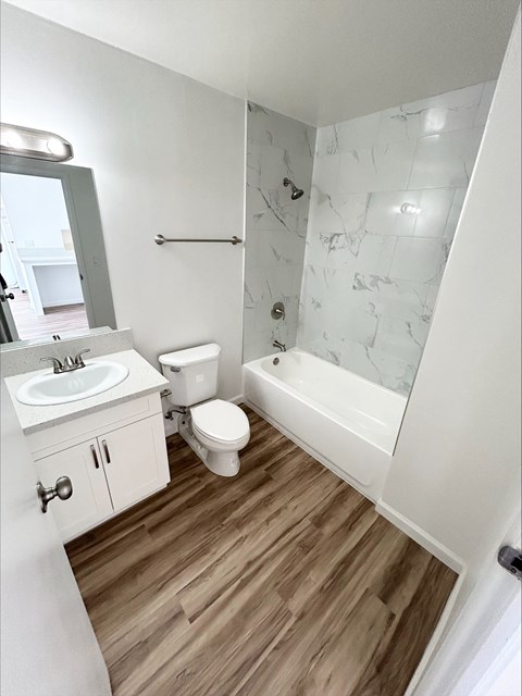 A white bathroom with a marble shower and wooden floors.