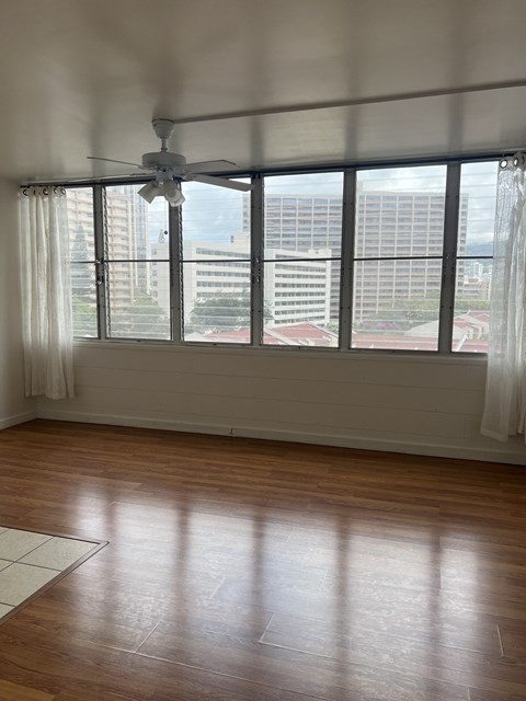 A room with a ceiling fan and a window overlooking a cityscape.