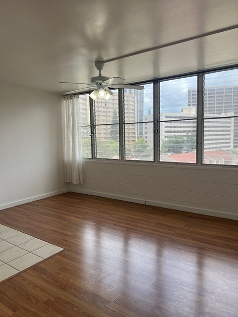 A room with a ceiling fan and a large window overlooking a cityscape.