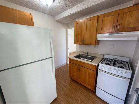 A white refrigerator sits next to a white stove in a kitchen with wooden cabinets.