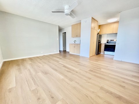 A room with wooden flooring and a kitchen area in the background.