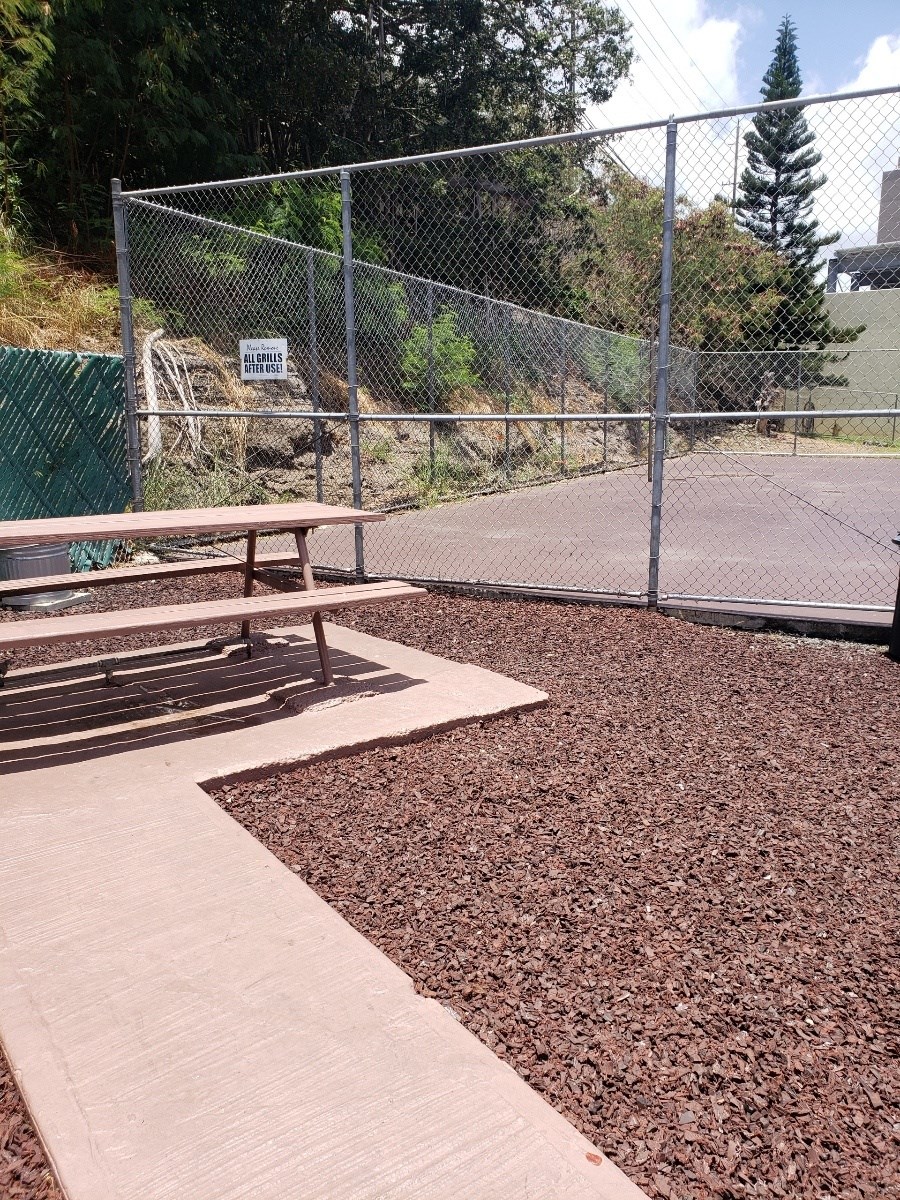 a picnic table in a fenced in area with a tennis court in the background