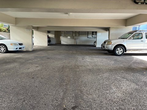 A car is parked in a garage with a white car to its left.