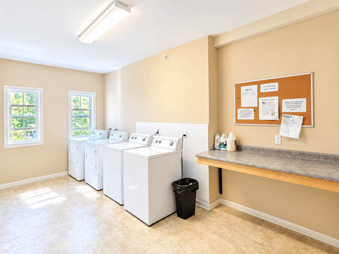 A laundry room with a washer and dryer, a trash can, and a bulletin board.